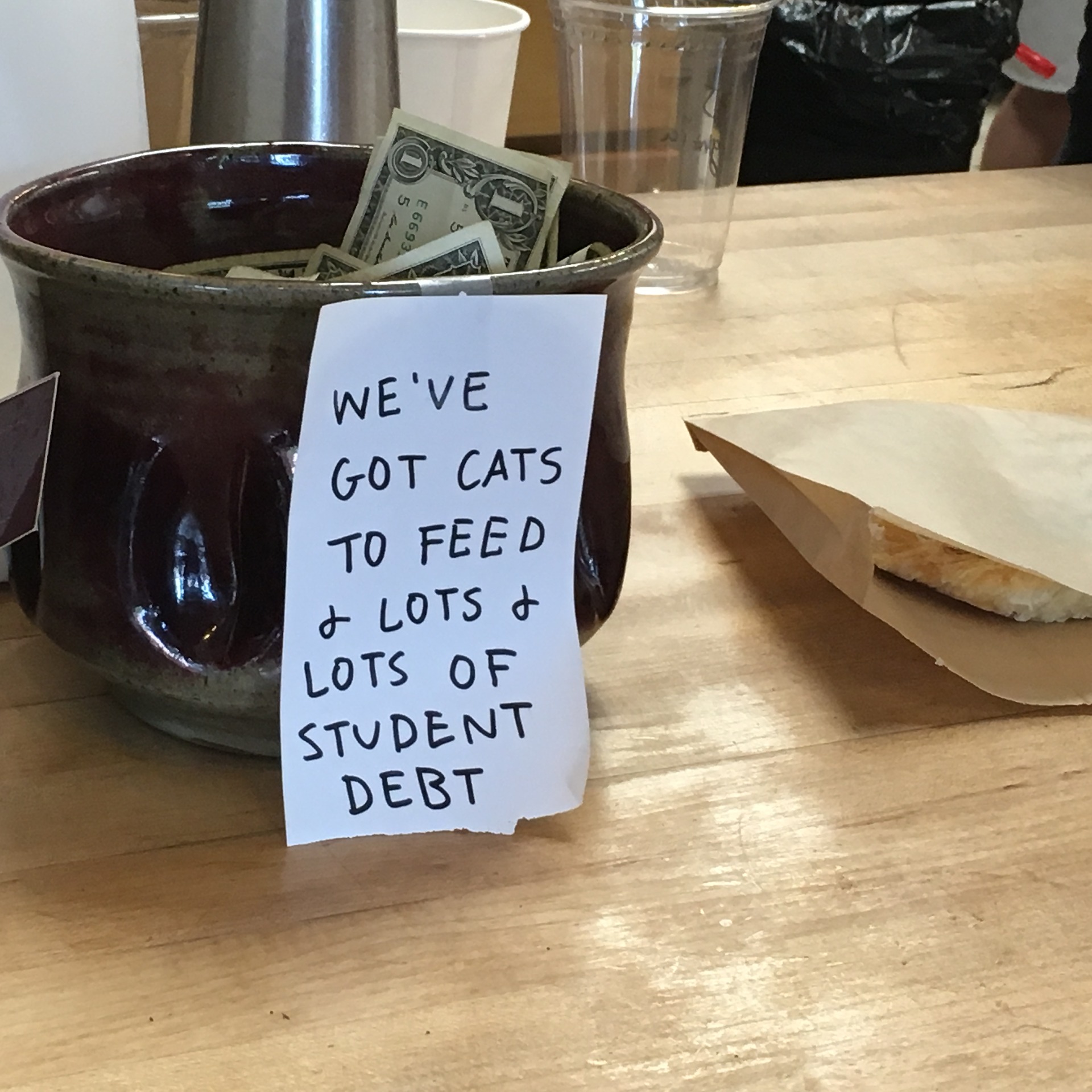 A jar holding dollar bills with a sign on it that reads "We've got cats to feed and lots and lots of student debt"