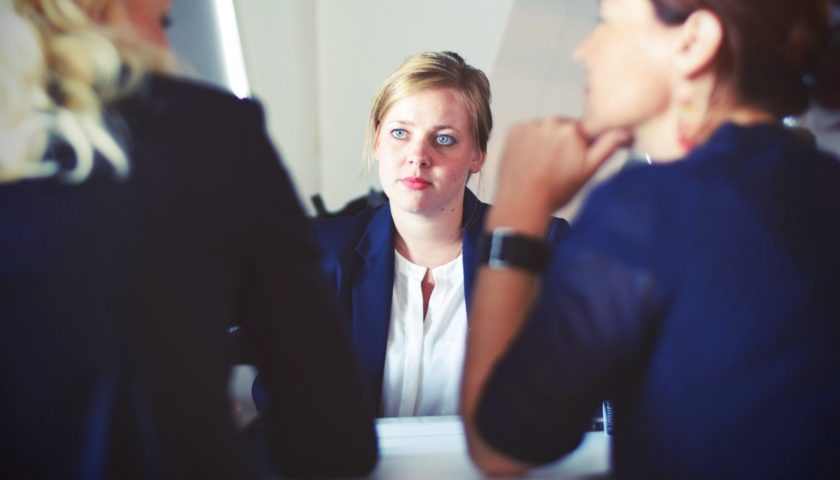 focus on girl sitting with blank stare on her face sitting in front of two women who appear to be interview the to other girl.