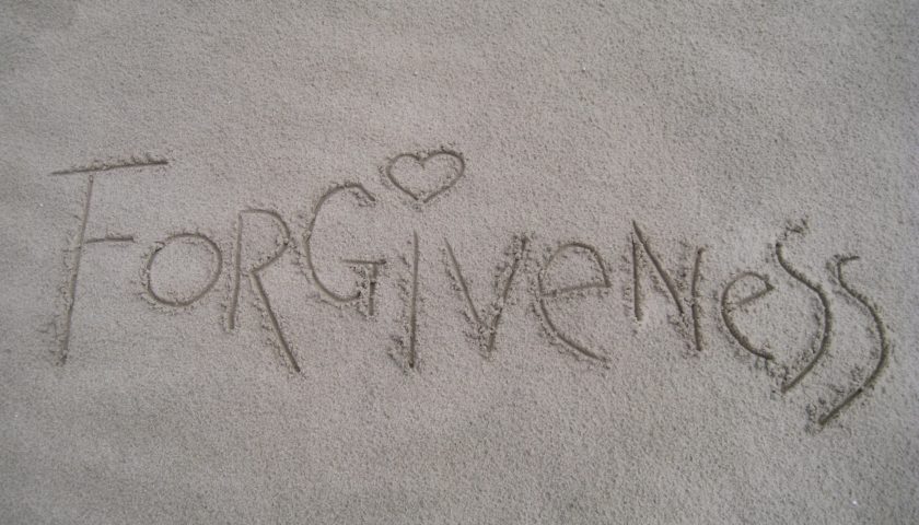 "forgiveness" written in sand with a heart for the dot over the "i"