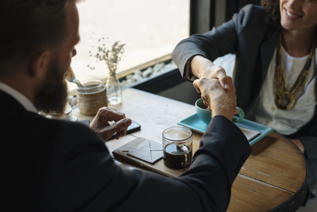 man and women in suits shaking hands with coffee in front of them