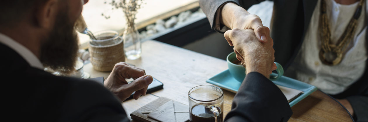 man and women in suits shaking hands with coffee in front of them