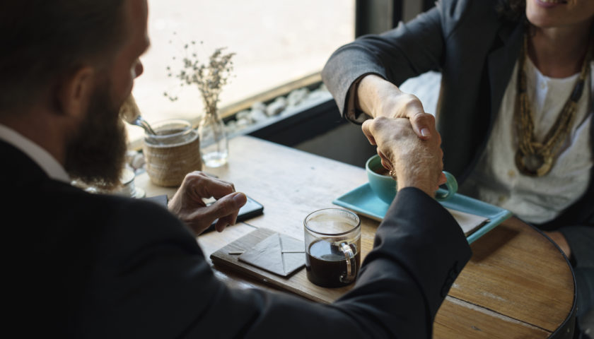 man and women in suits shaking hands with coffee in front of them