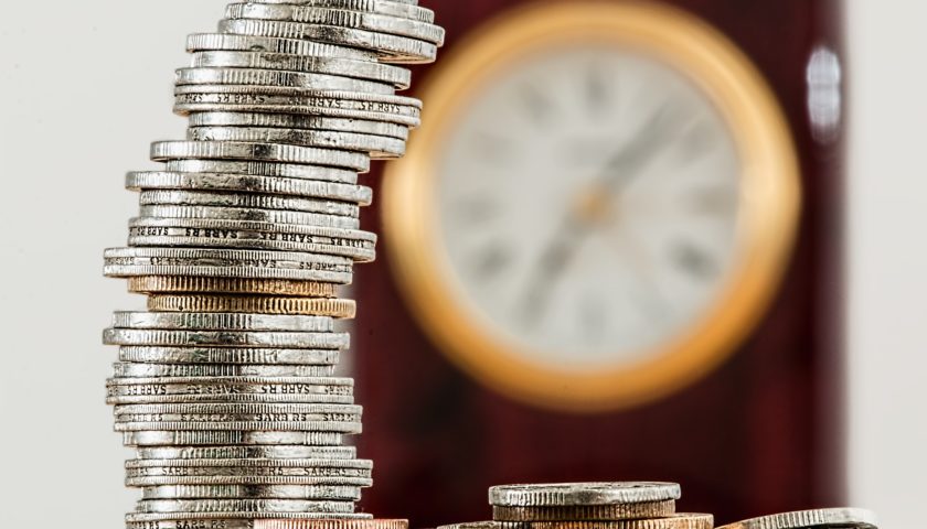 stack of coins in focus with clock in background that is out of focus