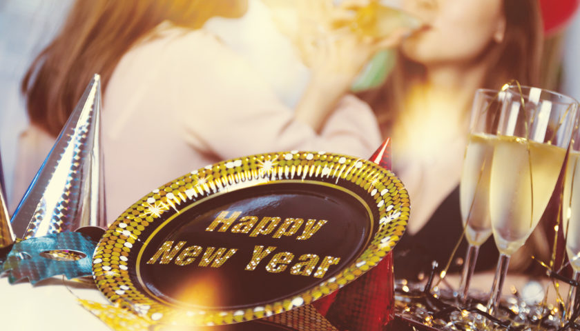 Happy new year written on plate with champagne glasses and to people in background sipping beverages