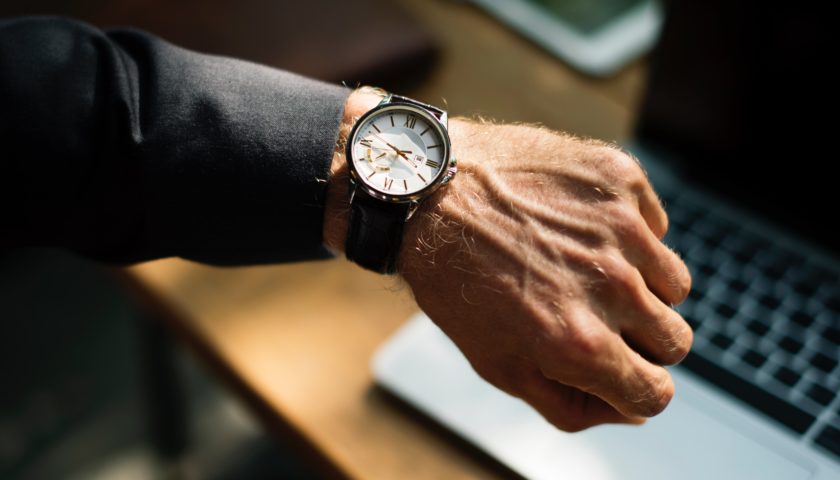 analog wrist watch on arm with laptop on desk in background