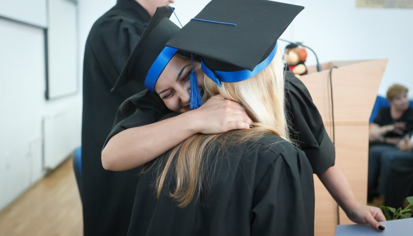 Two people in graduation cap and gown hugging