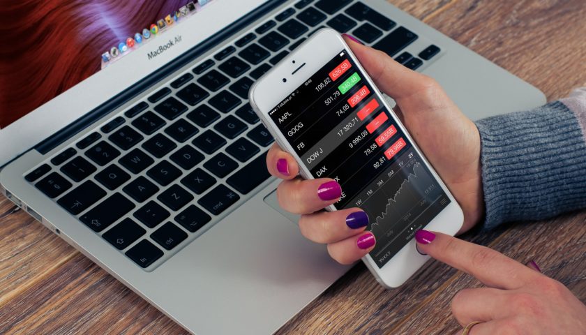 hands holding phone looking at stock market changes with a laptop in the background