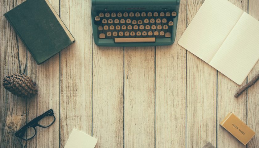 type writer, note pad, glasses on a wood surface