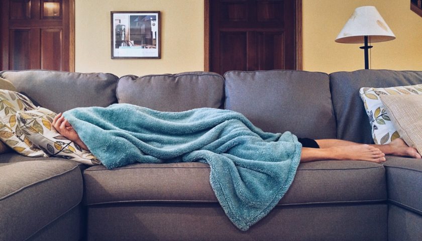person sleeping on couch with blanket over their head