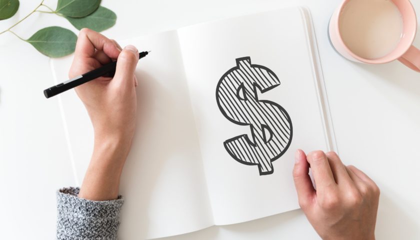 person with pen in hand drawing a dollar sign Photo by rawpixel on Unsplash