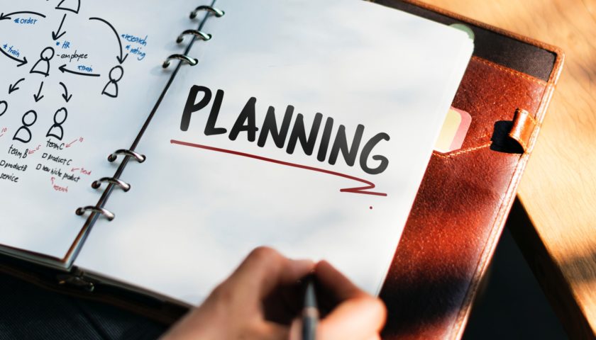 hand holding a pen on a planner with "planning" written in it