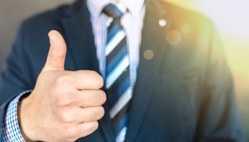 focus on thumbs up with background of person in suit blurry