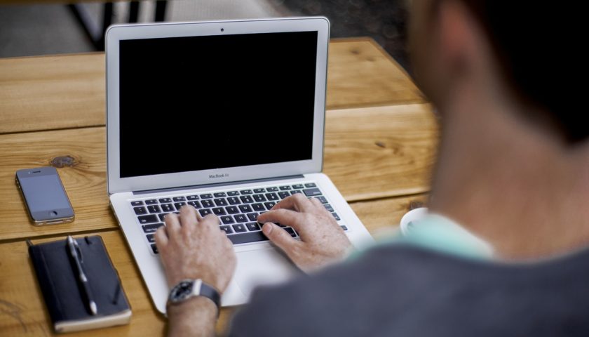 person typing on laptop sitting at a wood table