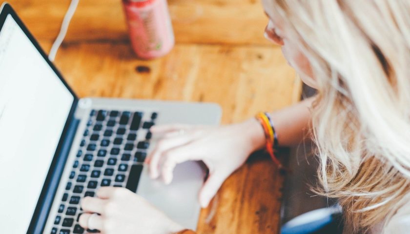 Blonde girl typing at a computer on a wood desk with a soda can