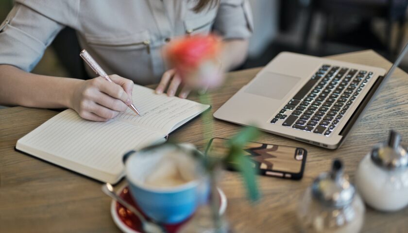 person writing on a notebook beside macbook