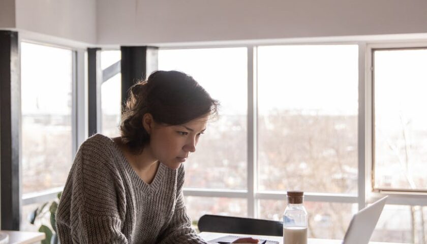 focused young woman using laptop in kitchen during breakfast