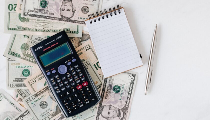 calculator and notepad placed over stack of usa dollars