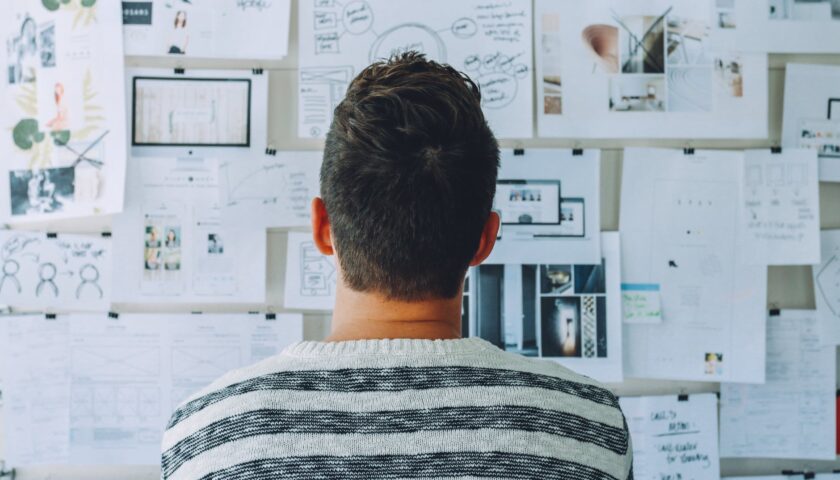 man wearing black and white stripe shirt looking at white printer papers on the wall